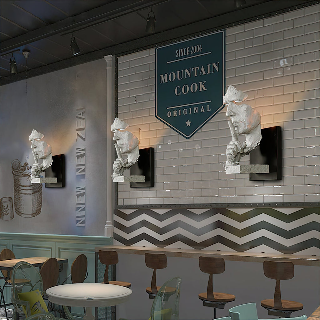 A row of Clérachic sculpted face wall lights above a counter in a cafe, set against a white brick wall.