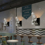 A row of Clérachic sculpted face wall lights above a counter in a cafe, set against a white brick wall.