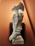 Close view of a white Clérachic face wall light, lit against a burnt-orange wall, with textured stone-like surface on the face and hand.