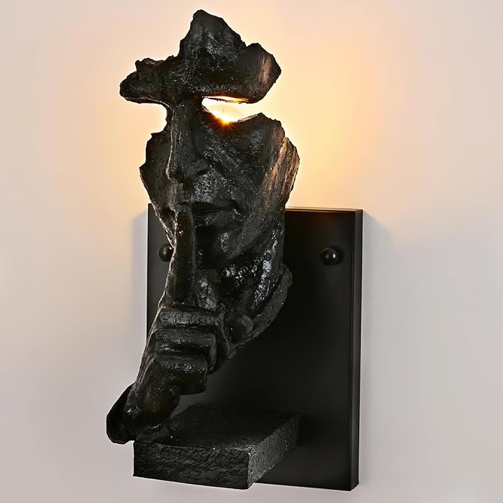 Close view of a black Clérachic face wall light with light shining from the eye gap and two screws visible on the plate.