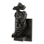 Black Clérachic face wall light photographed on white, showing the rough dark resin surface and the small shelf under the hand.