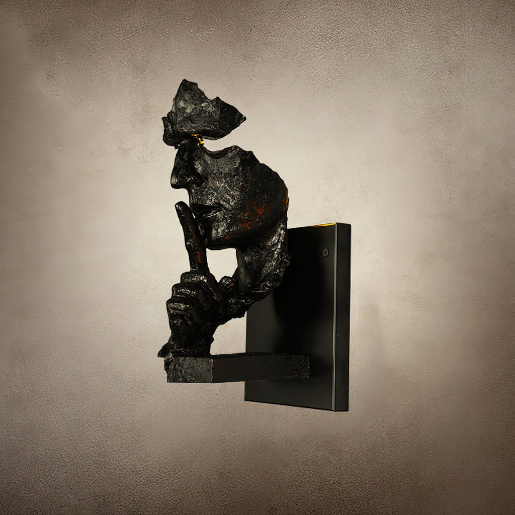 Side profile of a black Clérachic face wall light with specks of rust-orange, on a mottled beige backdrop.
