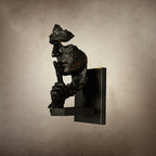 Side profile of a black Clérachic face wall light with specks of rust-orange, on a mottled beige backdrop.