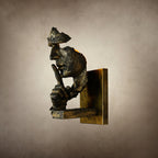 Side profile of a bronze Clérachic face wall light with a worn gold-toned plate, on a mottled beige backdrop.