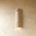 Clérachic arched wall light in cream travertine, its pitted natural stone texture visible, casting a warm pool of light downward.