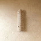 Clérachic elongated travertine wall light switched off, showing the porous cream stone and rounded top against a limewashed wall.