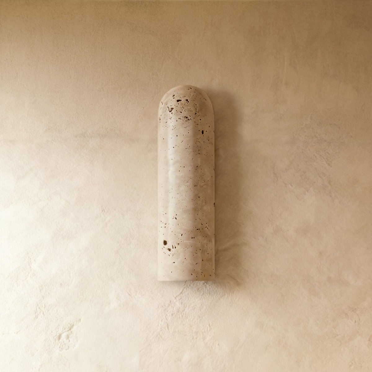 Clérachic elongated travertine wall light switched off, showing the porous cream stone and rounded top against a limewashed wall.