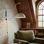 A white version of this Clérachic wall light on a painted brick wall, with a green armchair and a sloped timber ceiling.