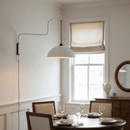 White domed shade on a slim swing arm, a Clérachic wall light beside a window, above a round table laid for dinner.