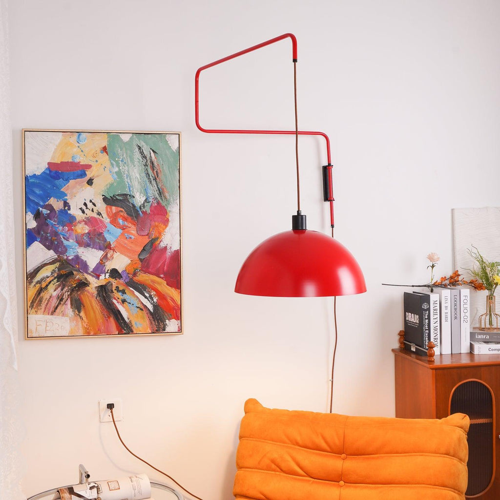 The red arm of this Clérachic wall light angles over a colourful abstract painting, with a wooden cabinet and orange sofa below.