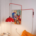 Shade pulled out to the left on this Clérachic wall light, its red arm stretched above a warm-lit orange sofa and painting.