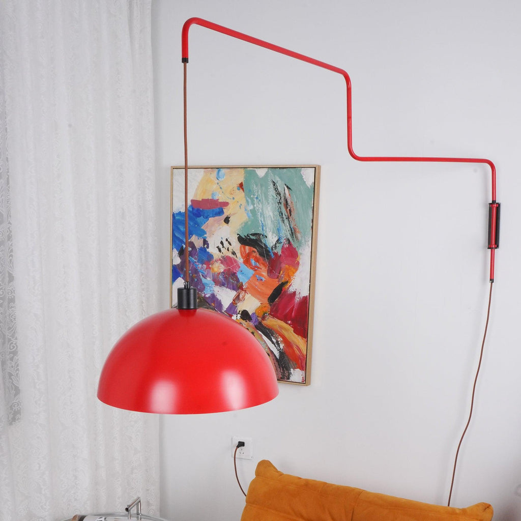 Close view of the red dome of this Clérachic wall light swung beside an abstract painting, with a black switch box on the stem.
