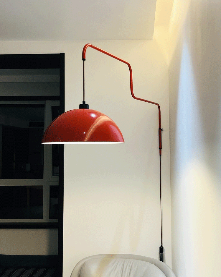 Smaller view of this Clérachic wall light in red against a cream wall, with a dark window frame and white chair beside.