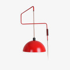 Red swing-arm wall light on a pale backdrop, with a glossy red shade and a brown cable, this Clérachic wall light shown flat on.