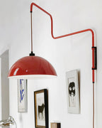 Close view of a glossy red shade on this Clérachic wall light, with framed prints hanging on the wall below.