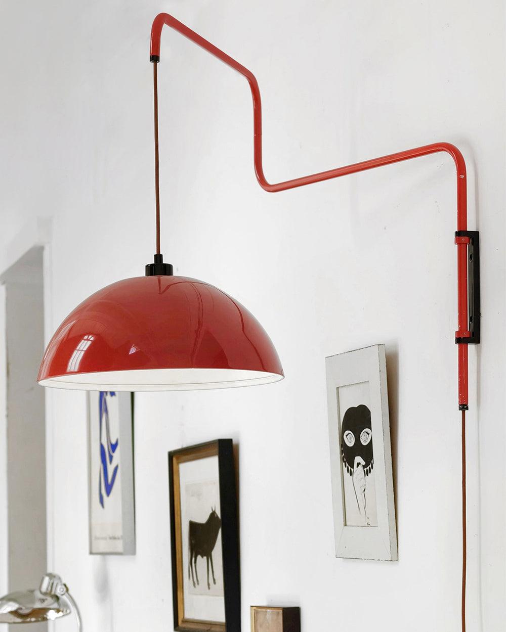 Close view of a glossy red shade on this Clérachic wall light, with framed prints hanging on the wall below.