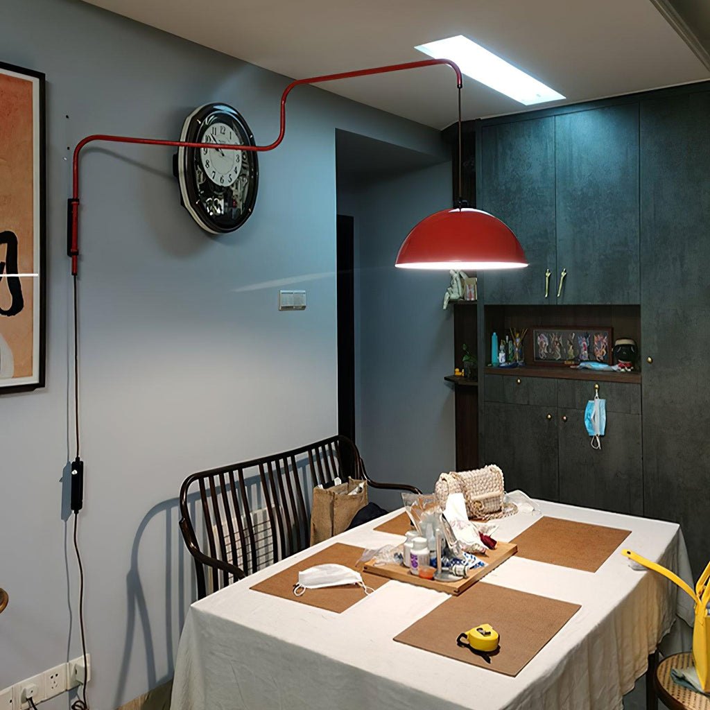 This Clérachic wall light in red lit above a dining table, with a wall clock and dark teal cabinets behind.