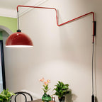 The red shade of this Clérachic wall light swung out above a plant-filled corner, on a cream wall with a window arch.