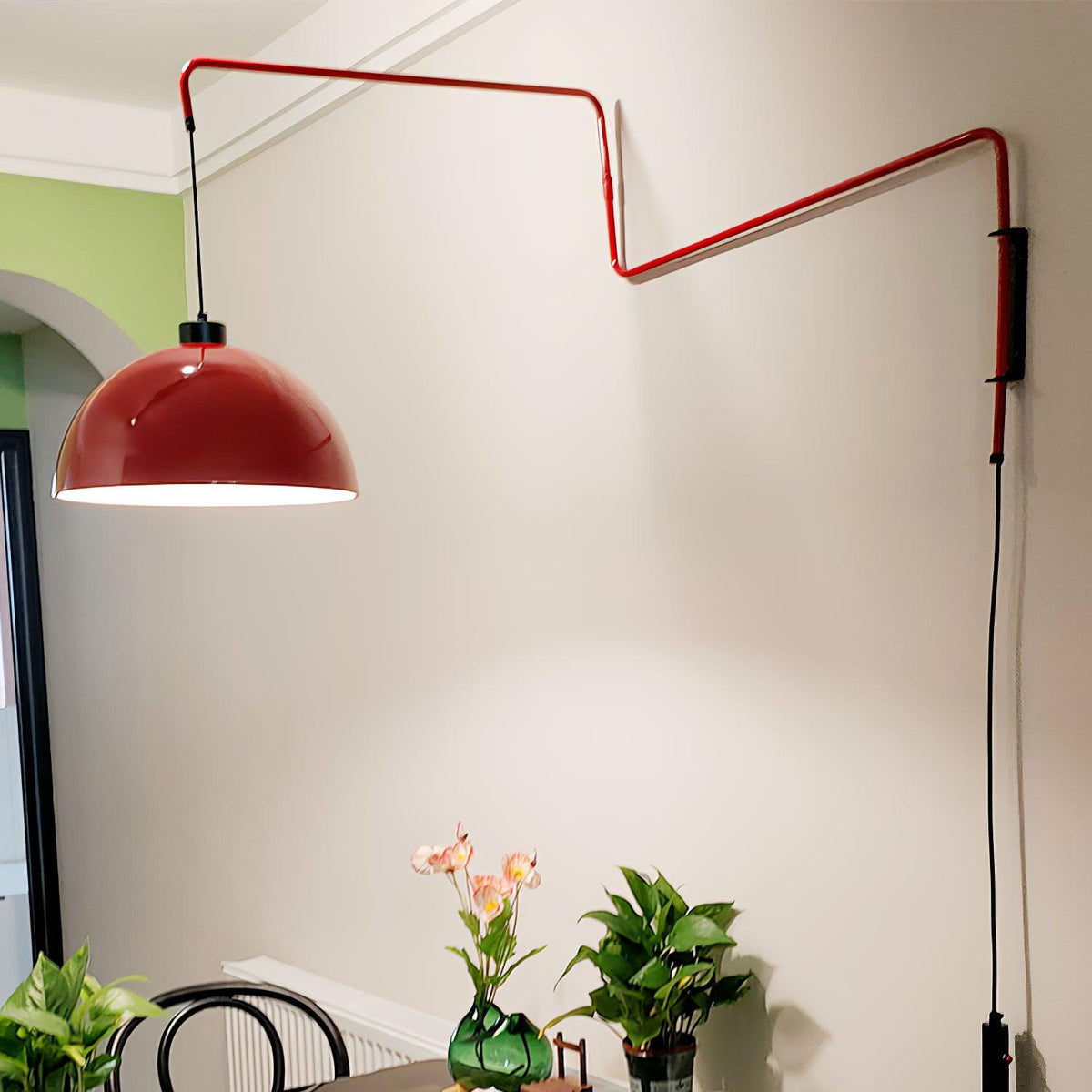 The red shade of this Clérachic wall light swung out above a plant-filled corner, on a cream wall with a window arch.