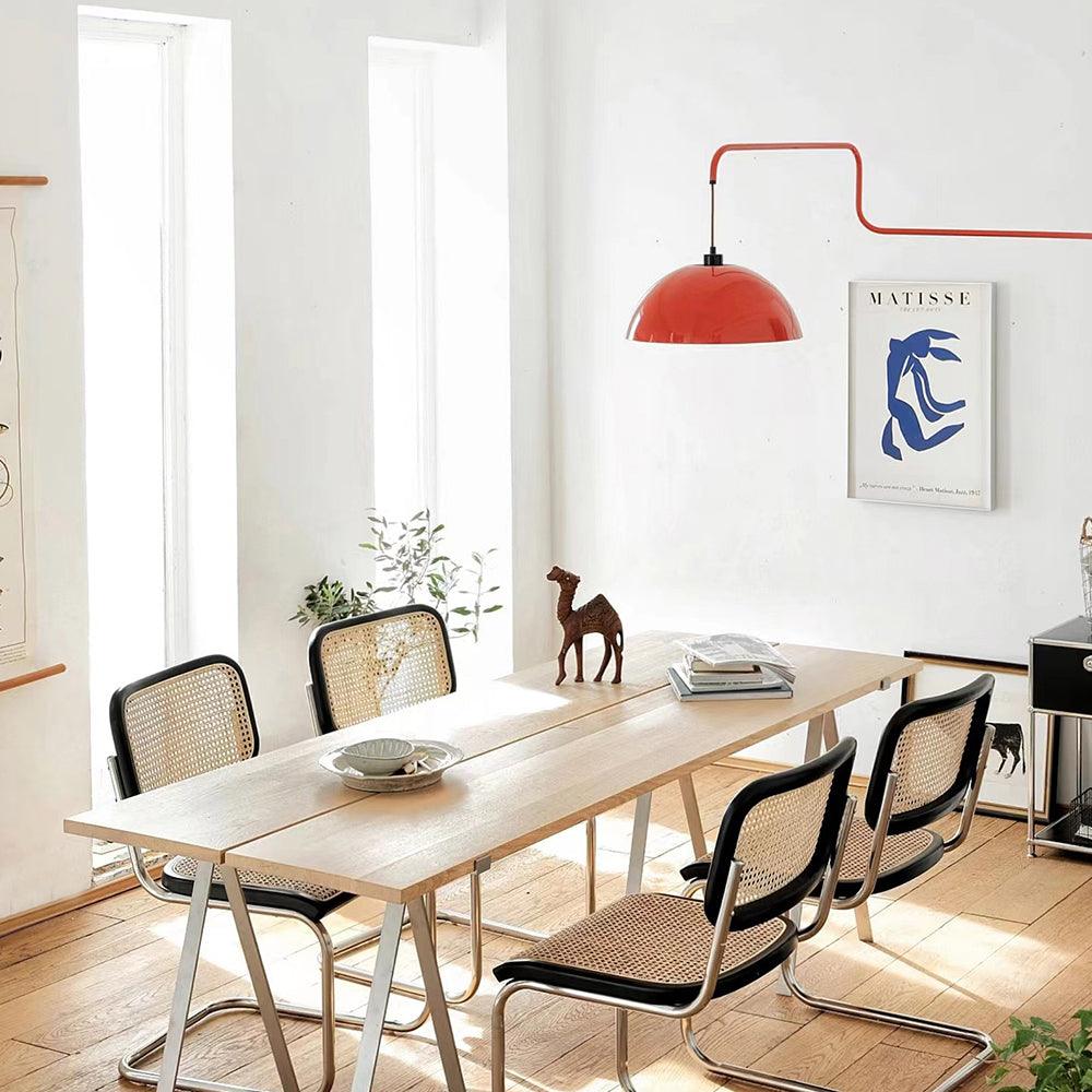 A red Clérachic wall light seen over a long pale wooden dining table with black cane-back chairs and a Matisse-style print.