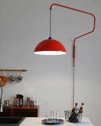 A red Clérachic wall light above a kitchen counter, with a brass rail of mugs, a bottle basket and glasses.