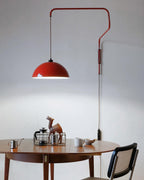 Dome of this Clérachic wall light lit over a round wooden table, with a cane chair, a cafetière and a camel figure below.