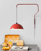 This Clérachic wall light in red above a dark desk, with a stack of books, an orange juice and a bowl of oranges.
