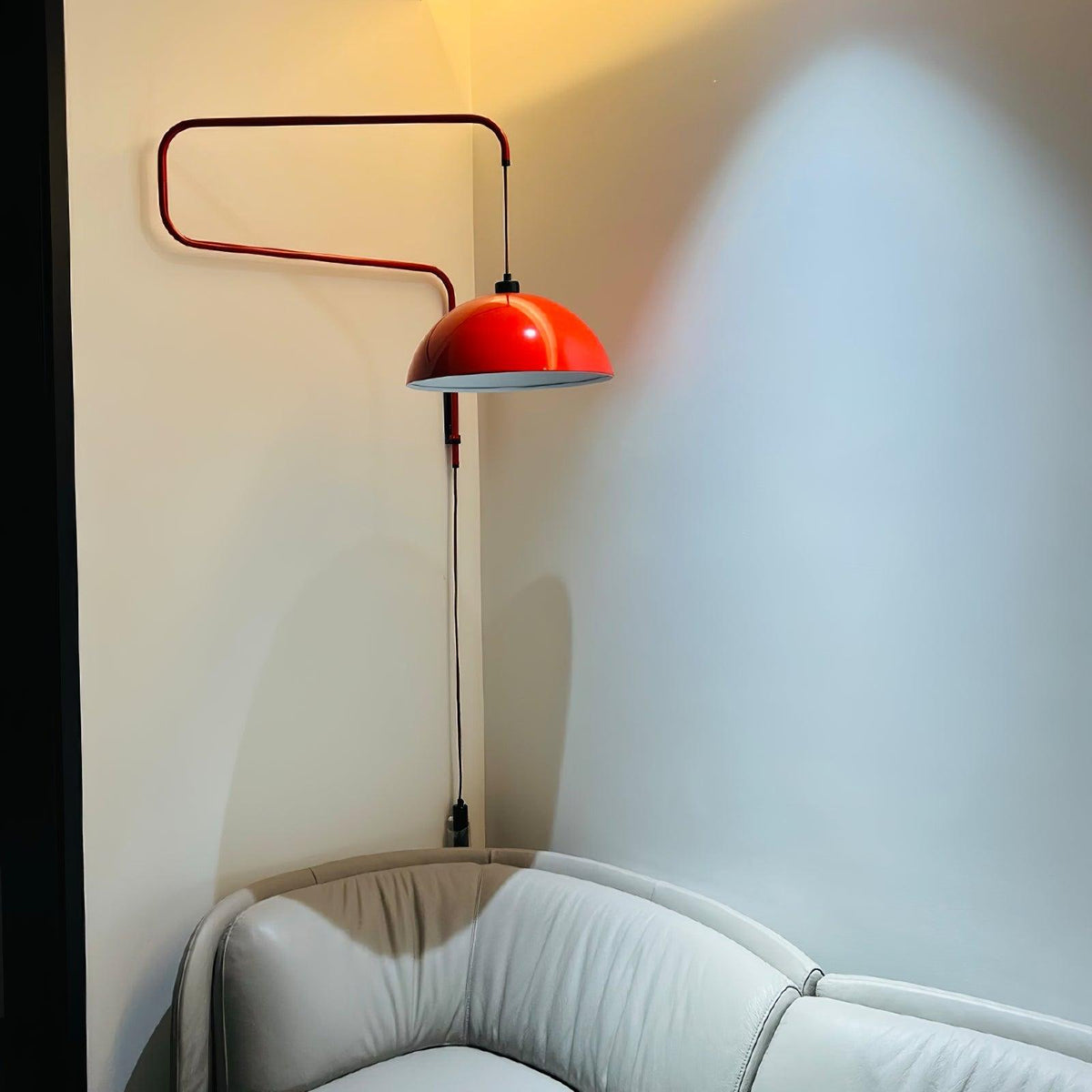 The red shade of this Clérachic wall light glows in a dim corner above a pale grey leather sofa.