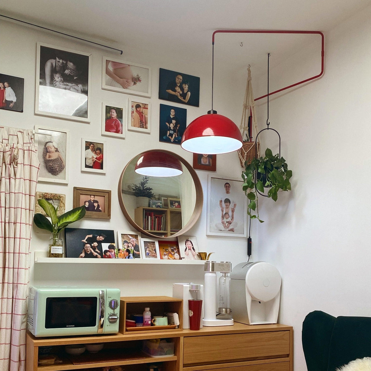 Red shade of this Clérachic wall light over a wall of framed photos, near a round mirror and a kitchen counter.