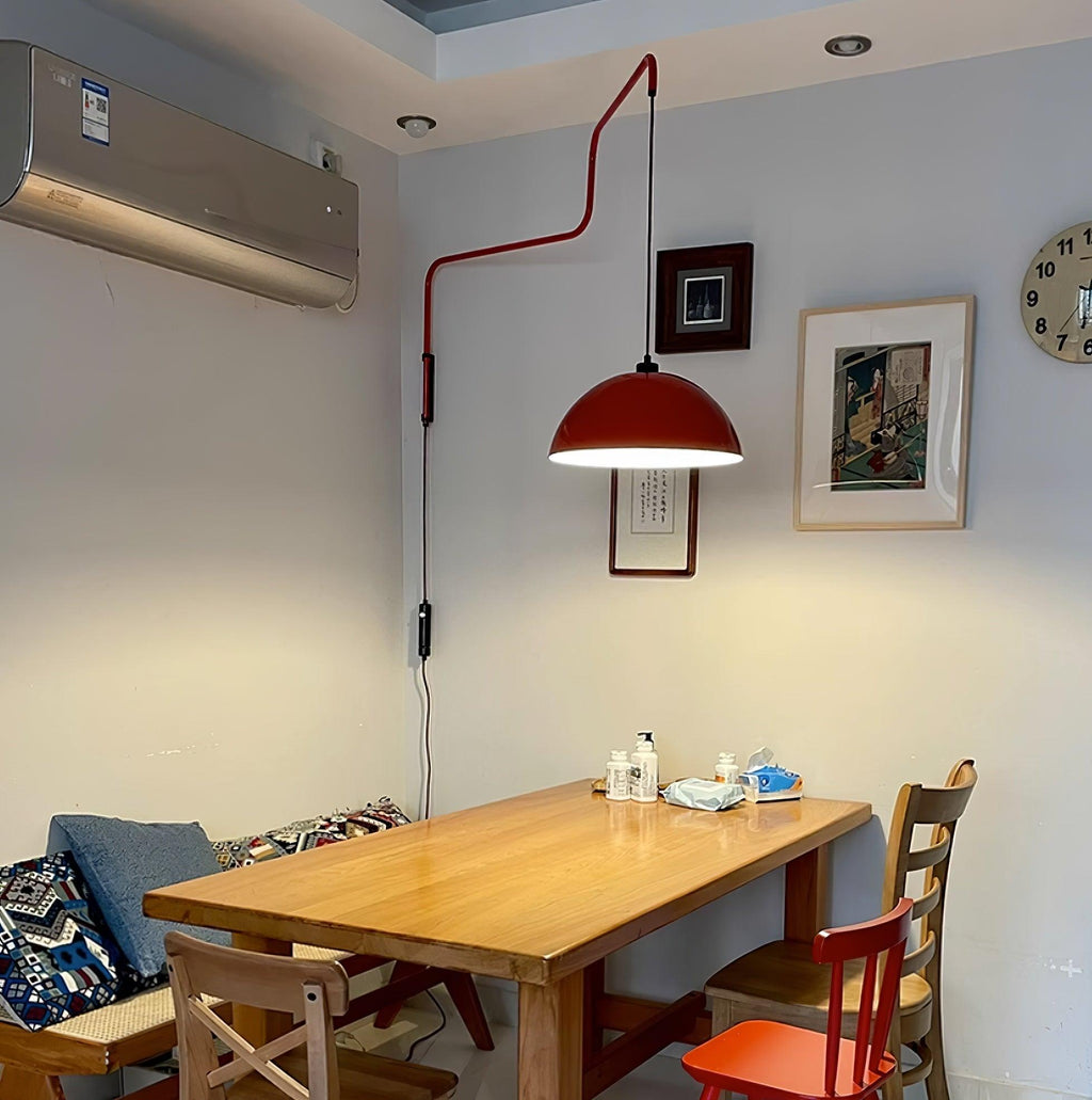 This Clérachic wall light in red hangs above a wooden dining table in a room with an air-conditioner and wall clock.