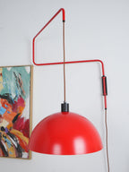 Red domed shade of this Clérachic wall light swung in front of an abstract painting, on a white-grey wall.