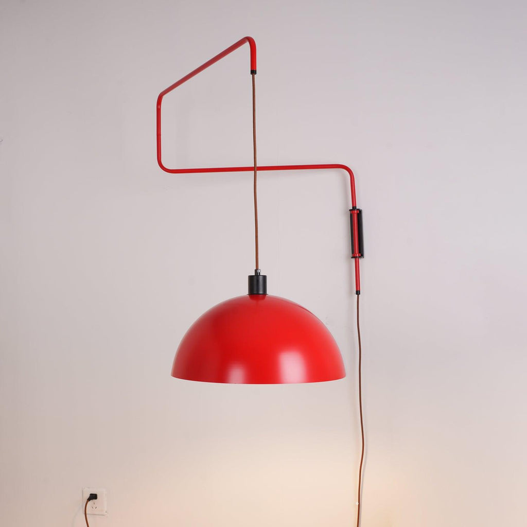 Zigzag arm and red shade of this Clérachic wall light on a soft grey wall, with a wall socket at lower left.