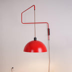 Zigzag arm and red shade of this Clérachic wall light on a soft grey wall, with a wall socket at lower left.