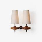 Front view of a Clérachic twin-shade wall sconce with two cream fabric shades above walnut-toned wooden discs, on a plain white backdrop.