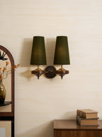 Twin dark-green shades glow softly on this Clérachic wall sconce, mounted on a cream wall beside an arched mirror and a walnut cabinet.