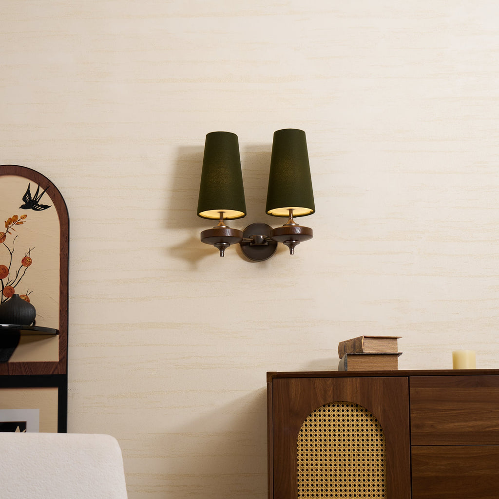 Lit from below, the two green shades of this Clérachic sconce throw warm light on a cream wall above a cane-fronted walnut sideboard.