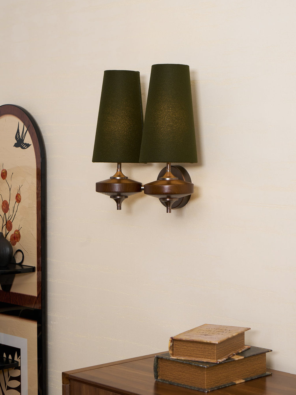 Angled view of a Clérachic wall sconce with two green shades, its bronze round backplate and walnut discs seen from the side.