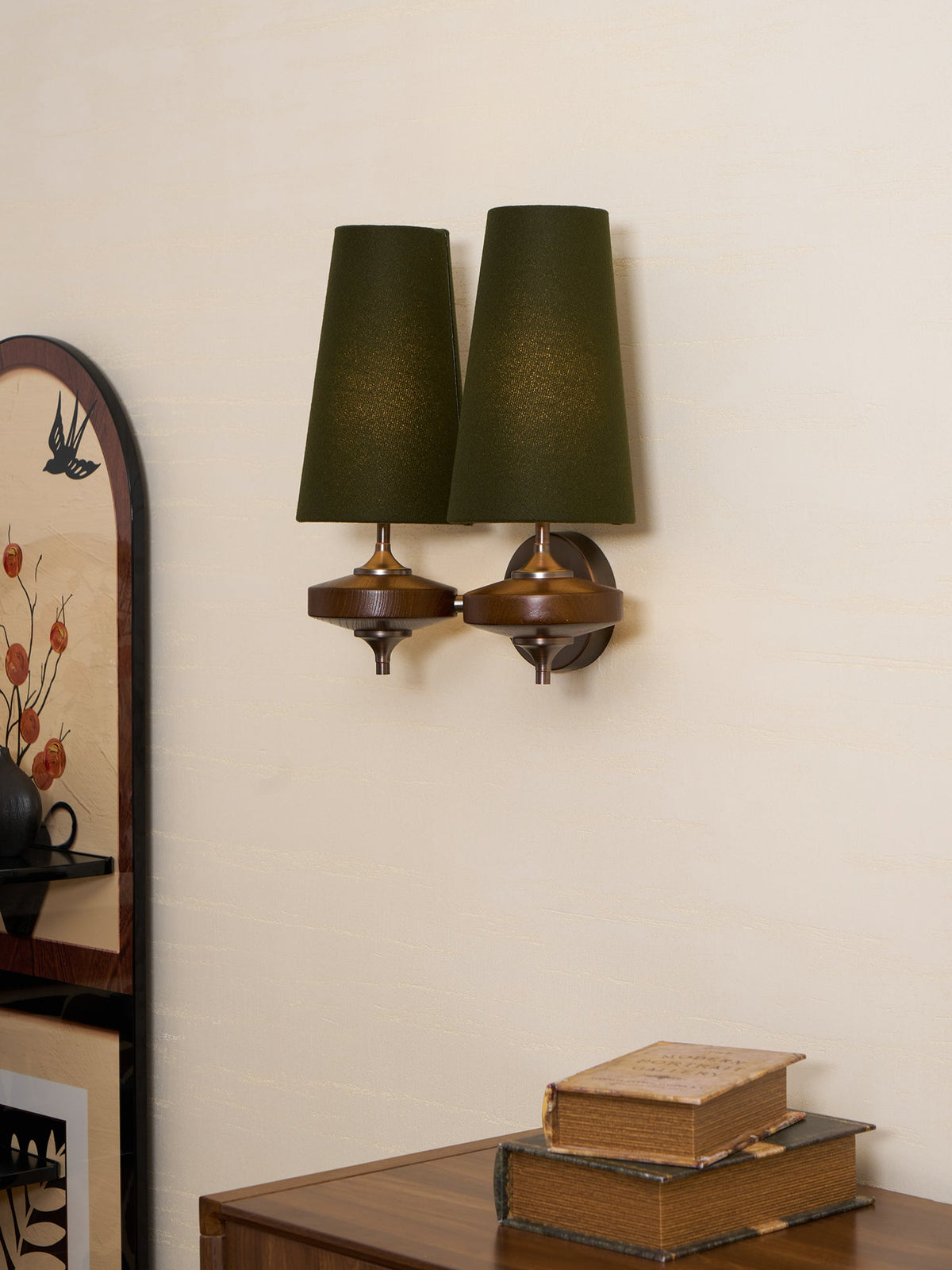 Angled view of a Clérachic wall sconce with two green shades, its bronze round backplate and walnut discs seen from the side.