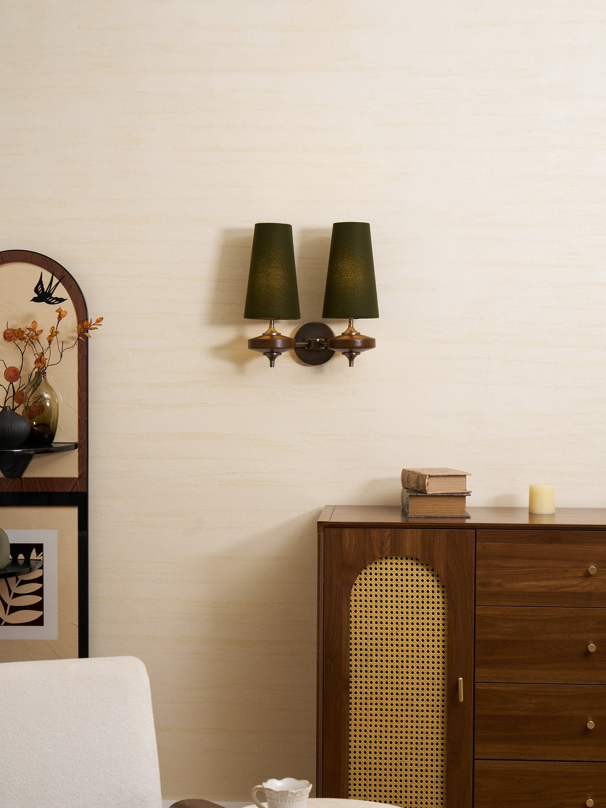 Small in the frame, this Clérachic green-shaded sconce hangs high above a cane-doored cabinet and a cream armchair.