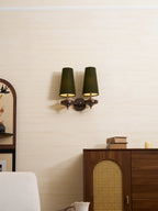 A Clérachic twin sconce with green shades lit warm from within, set above a rattan-panelled cabinet and a pale armchair.