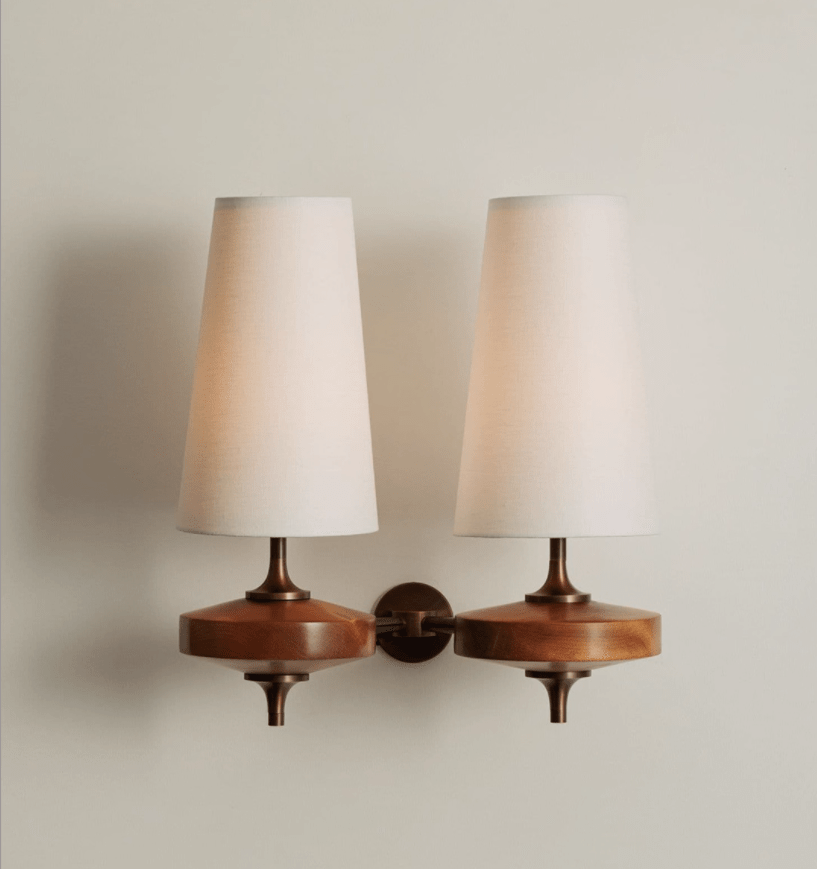 Cream fabric shades and walnut wood bases on a Clérachic twin wall sconce, shown on a soft grey wall with bronze stems.