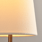 Close view of the woven cream fabric shade glowing from inside on this Clérachic wall sconce, with a bronze stem beneath.