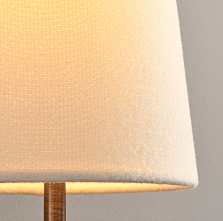 Close view of the woven cream fabric shade glowing from inside on this Clérachic wall sconce, with a bronze stem beneath.