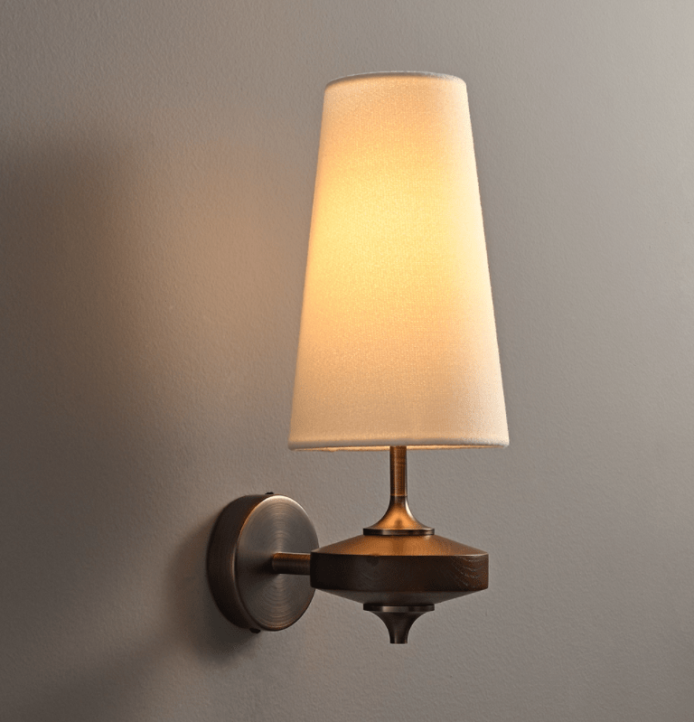 A single cream shade lit warm above a dark wood disc and round bronze backplate on a Clérachic wall sconce, against a grey wall.