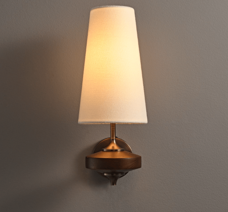 Warm light fills the cream shade of this Clérachic wall sconce, mounted on a deep grey wall above its walnut disc.