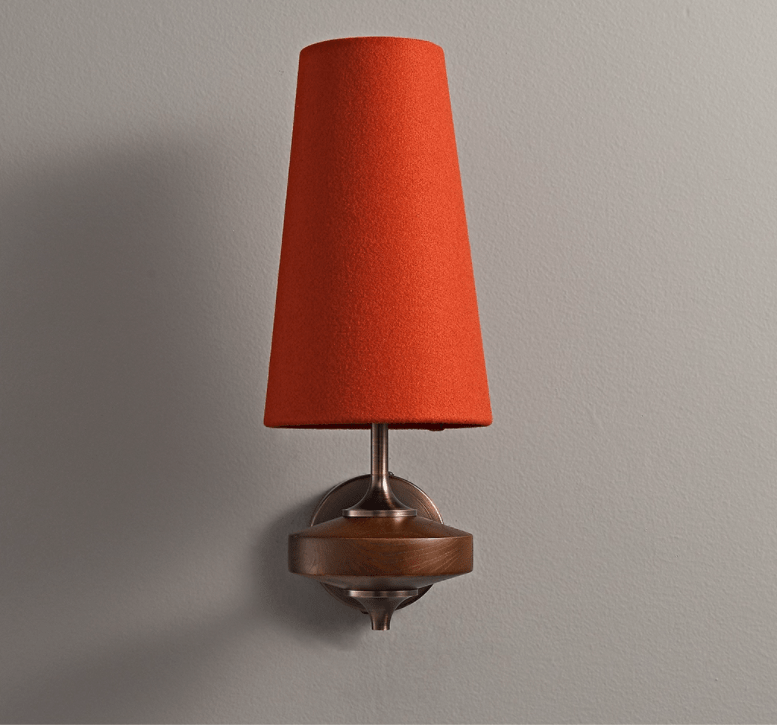 A red fabric shade on a Clérachic single-arm wall light, with the walnut disc and bronze backplate below, on grey.