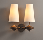Both white shades glowing on a Clérachic twin wall sconce, joined by a bronze backplate with a chain-link arm, on grey.
