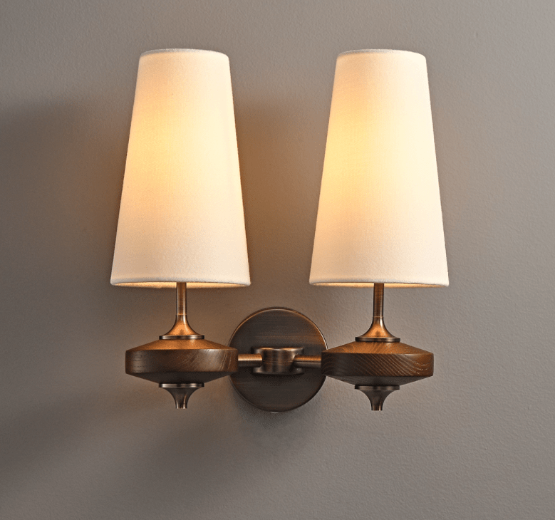 Both white shades glowing on a Clérachic twin wall sconce, joined by a bronze backplate with a chain-link arm, on grey.
