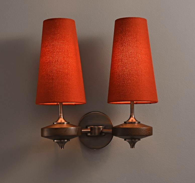 Two lit red shades on a Clérachic twin sconce, their warm glow reaching the bronze stems and walnut discs below.
