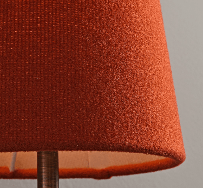 Close view of the textured red wool-like fabric of a lit shade on this Clérachic wall sconce, with its bronze stem below.